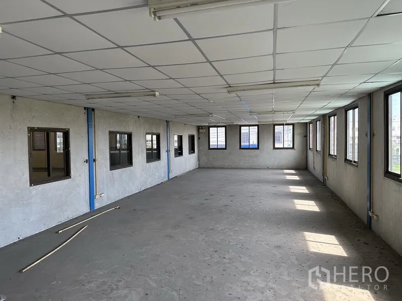 Warehouse for rent in Bang Phli, Samut Prakan - Another bright office room with tiled ceiling panels, multiple windows, and raw concrete floors.