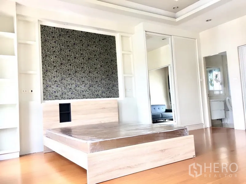 Townhouse for rent in Prawet, Bangkok - A spacious bedroom featuring a patterned headboard wall, shelving and a sliding wardrobe.