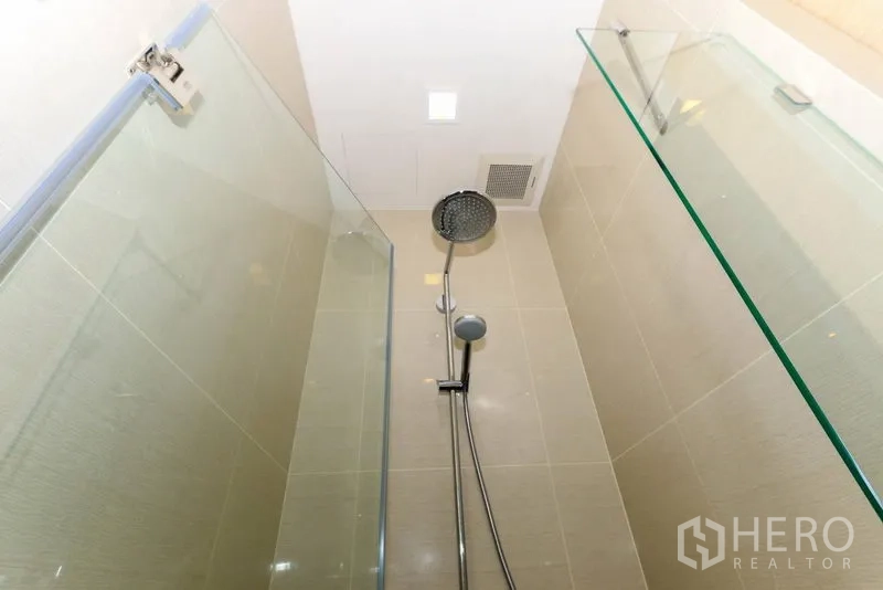 Condominium for rent in Khlong Toei, Bangkok - Glass-enclosed bathroom with rain showerhead and handheld spray over neutral tiles.