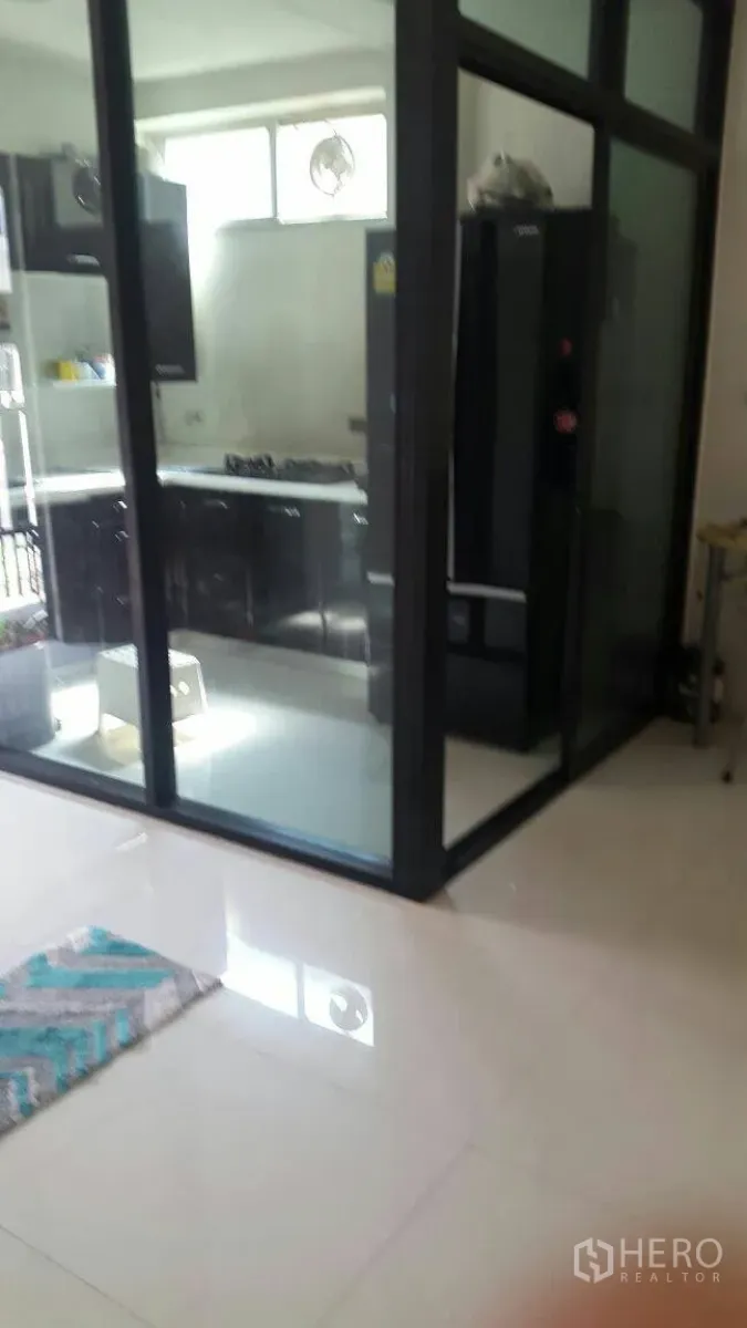 Townhouse for rent in Suan Luang, Bangkok - Glass-enclosed kitchen with black cabinets, gas cooktop and a large fridge at Noble Cube Suan Luang.