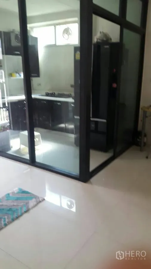 Townhouse for rent in Suan Luang, Bangkok - Glass-enclosed kitchen with black cabinets, gas cooktop and a large fridge at Noble Cube Suan Luang.