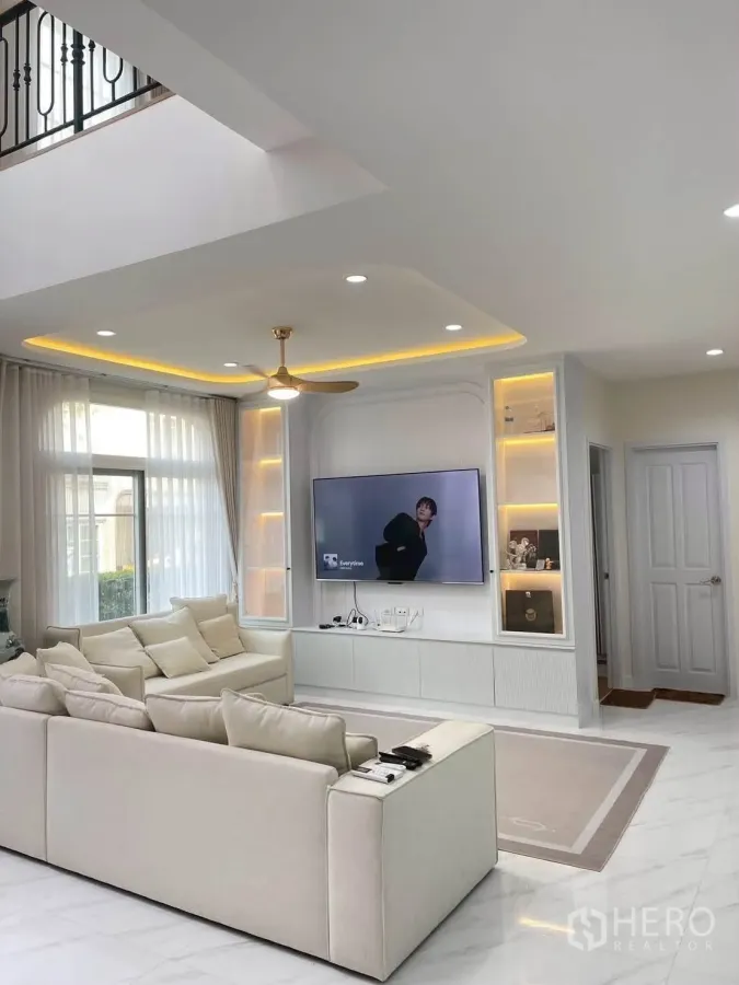 บ้านเดี่ยว for rent or sale in Bang Phli, Samut Prakan - ห้องนั่งเล่นมีโซฟารูปตัวแอล ชั้นโชว์ไฟในตัว และทีวีติดผนัง.