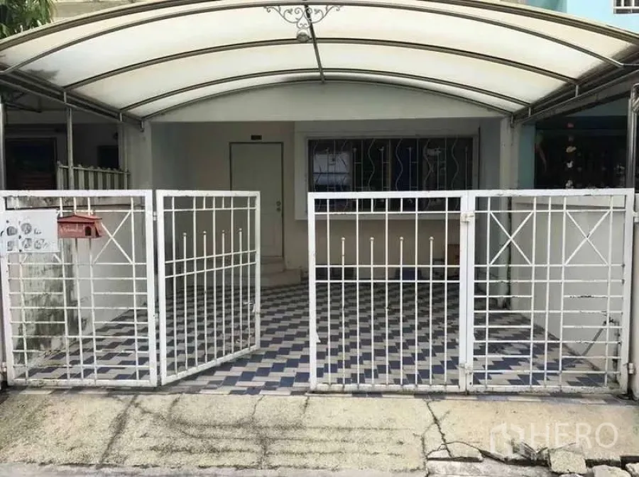 Townhouse for rent in Suan Luang, Bangkok - Townhouse front exterior with white metal gate, covered carport and checkered tile floor.