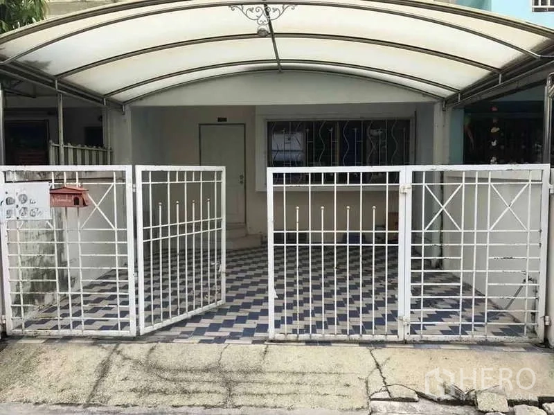 Townhouse for rent in Suan Luang, Bangkok - Townhouse front exterior with white metal gate, covered carport and checkered tile floor.