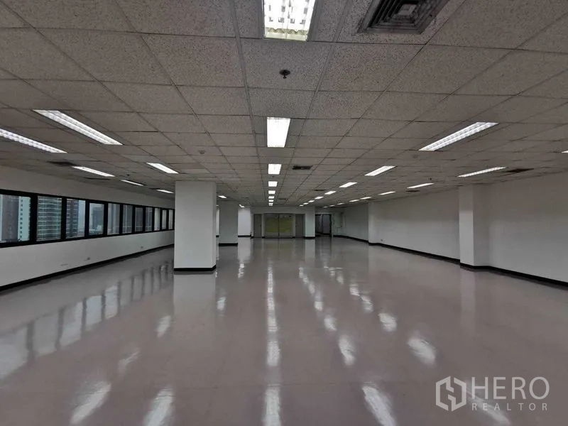 Office Space for rent in Watthana, Bangkok - Central perspective of a large empty office with fluorescent lighting and an entire wall of windows.