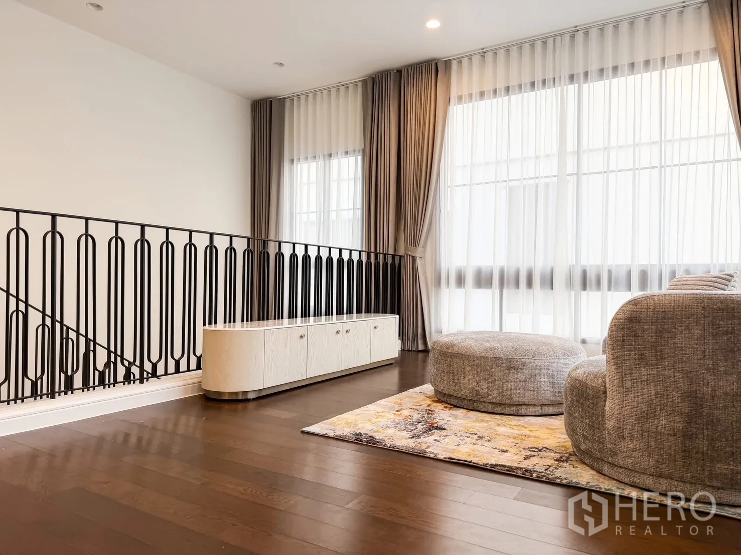 Detached House for rent in Bang Khen, Bangkok - Upper hall seating area with decorative iron railing, media console and round ottoman.