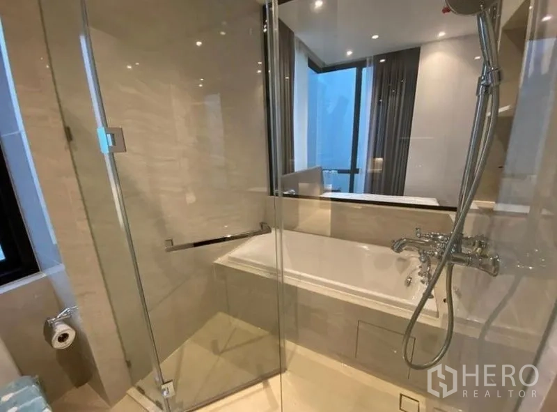 Condominium for rent in Pathum Wan, Bangkok - Modern bathroom with glass shower enclosure, separate bathtub, and chrome fixtures near a window.