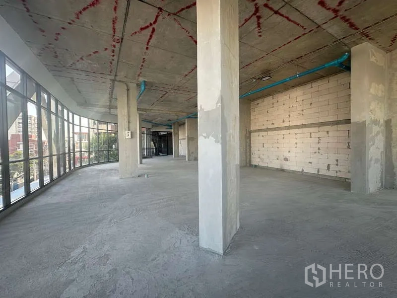 Retail Space for rent in Phra Khanong, Bangkok - Wide retail floor showing curved window line, concrete columns, and marked unfinished ceiling.
