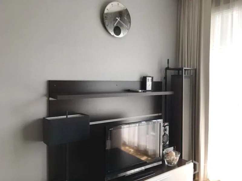 Condominium for rent in Khlong Toei, Bangkok - Bright living area featuring TV console, floating shelves, floor lamp, wall clock and sheer curtains.