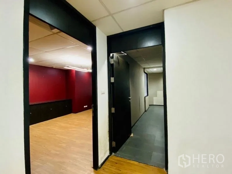 Office Space for rent or sale in Watthana, Bangkok - Hallway to an office room with red accent wall, wood floors and black door frames.