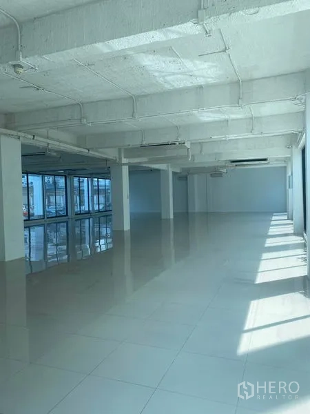 Office Space for rent in Khlong Toei, Bangkok - Open office area with rows of windows, sunlight streaming in, exposed piping ceiling and glossy floor.