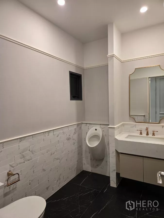 Detached House for rent or sale in Bang Kapi, Bangkok - Guest bathroom with marble wall tiles, vanity, toilet and urinal.