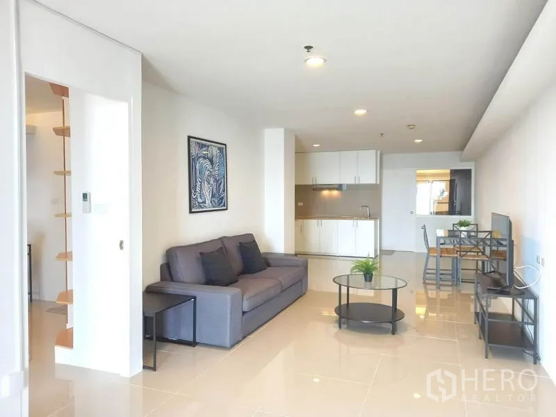 Condominium for rent in Khlong Toei, Bangkok - Living area facing compact white kitchen and dining table in a bright space.
