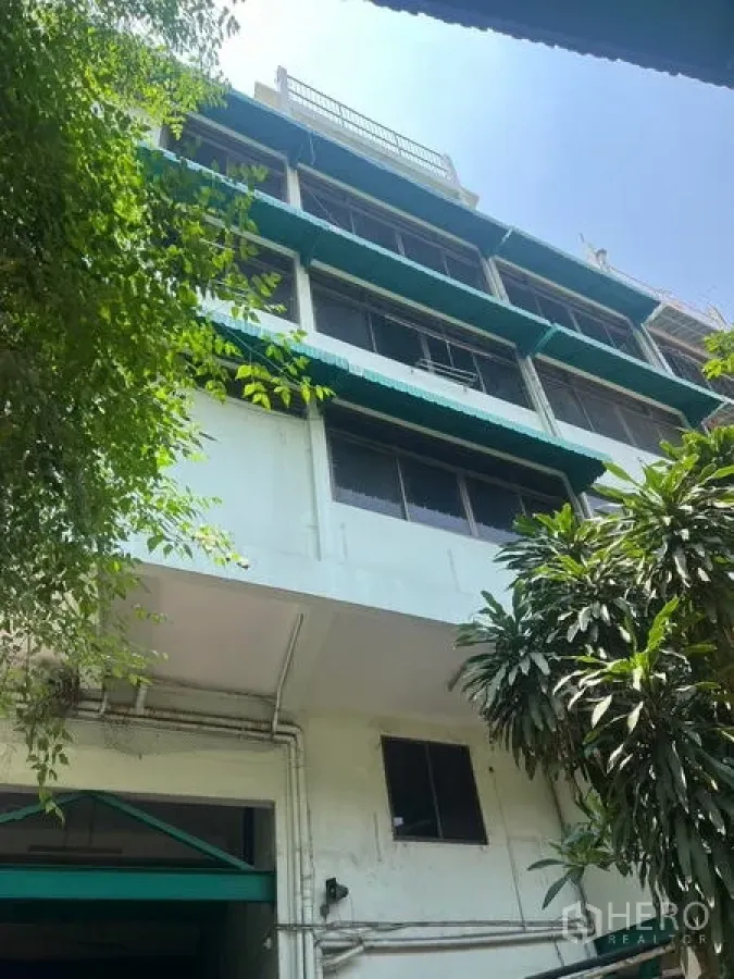 Warehouse for rent in Bang Kho Laem, Bangkok - Multi-storey warehouse-office exterior with green awnings and foliage.