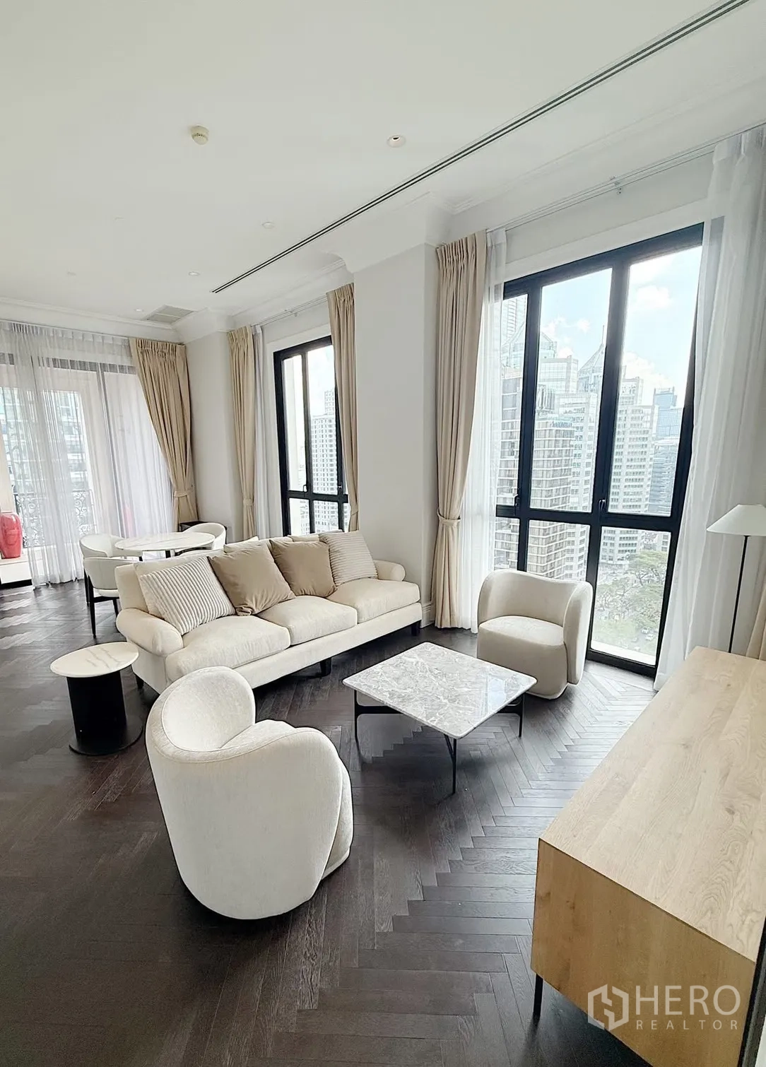Condominium for rent or sale in Pathum Wan, Bangkok - Bright lounge with soft-toned furniture, herringbone wood flooring, and panoramic city views.