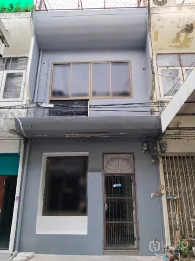 Shophouse for rent in Watthana, Bangkok - Two-storey shophouse exterior with wide front window and metal gate in an urban row.