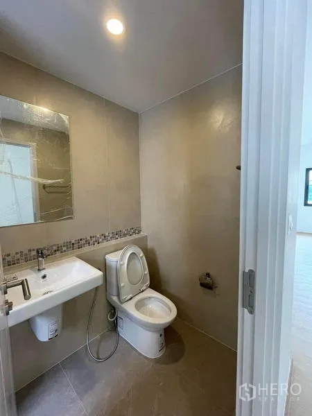 Townhouse for rent in Prawet, Bangkok - Compact bathroom featuring a toilet, square sink, mirror and neutral tiled walls.