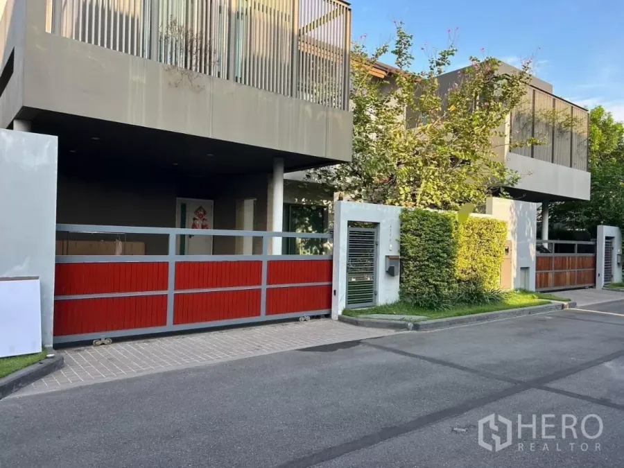 Detached House for rent in Bang Kapi, Bangkok - Modern two-storey detached house facade with red sliding gate, balcony screens and greenery.