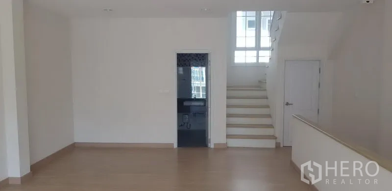 Townhouse for rent in Bang Na, Bangkok - Open plan level featuring light wood floors, a staircase with window, and an internal bathroom door.