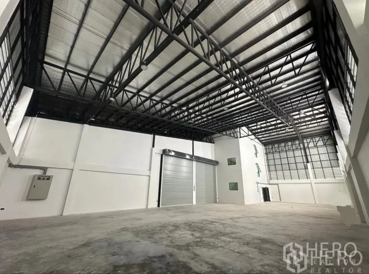 Warehouse for sale in Lam Luk Ka, Pathum Thani - Spacious warehouse interior with high steel truss roof, insulated panels and polished concrete floor, plus large roller shutter.