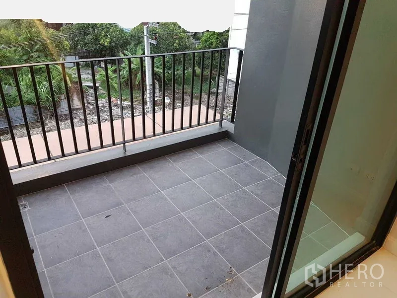 Shophouse for rent or sale in Bang Na, Bangkok - Private balcony with gray floor tiles and black railing overlooking greenery.