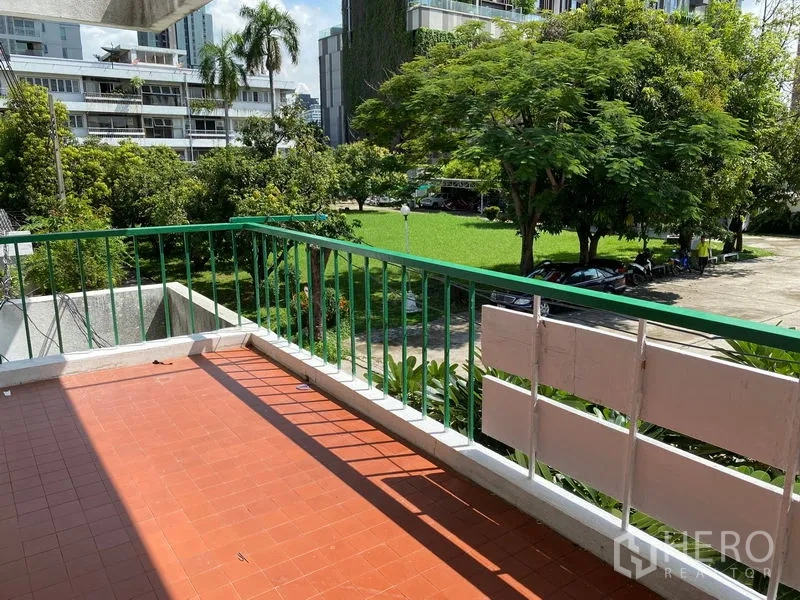 Apartment for rent in Khlong Toei, Bangkok - Sunny balcony with terracotta tiles overlooking green garden and low-rise buildings.