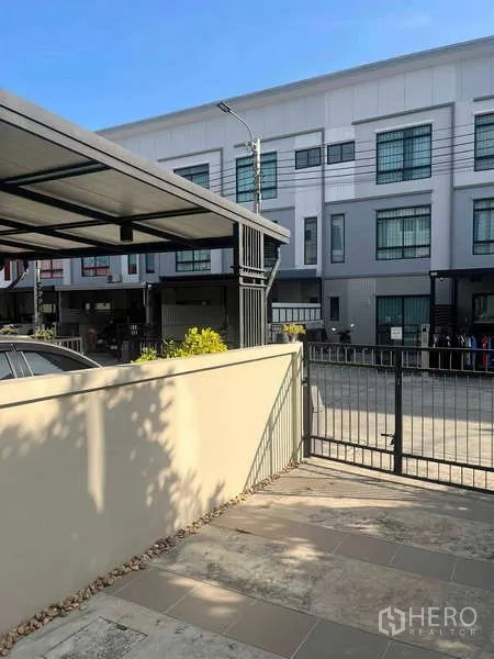 Townhouse for rent in Suan Luang, Bangkok - Gated front patio of the townhouse facing a row of neighboring townhomes and a covered carport.