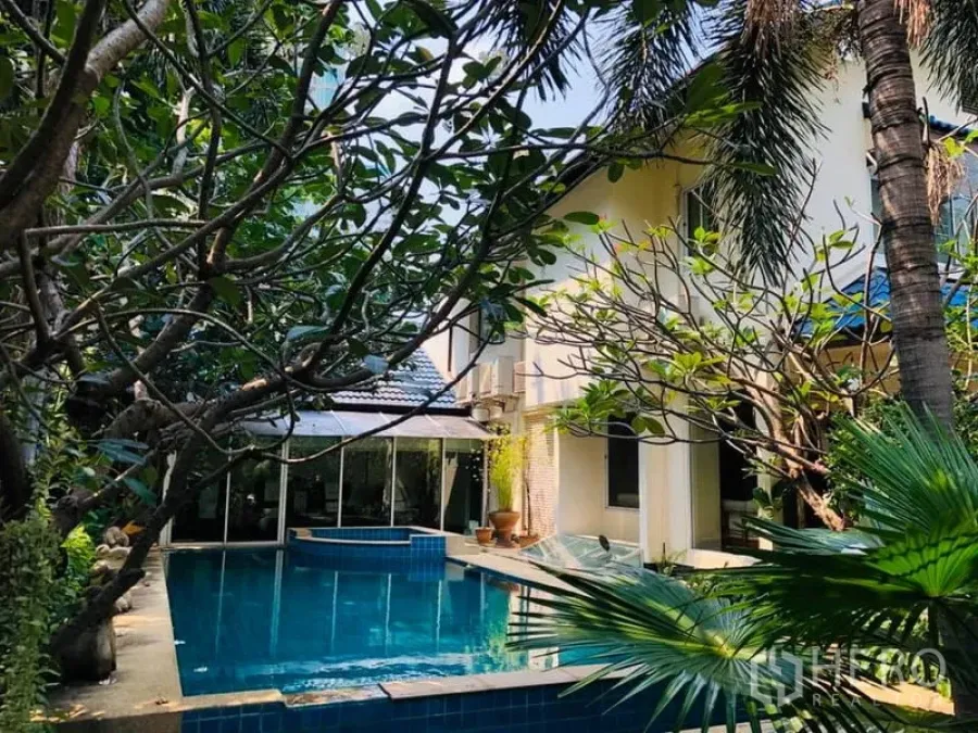 Detached House for rent in Khlong Toei, Bangkok - Poolside view of the residence framed by frangipani and palm trees.