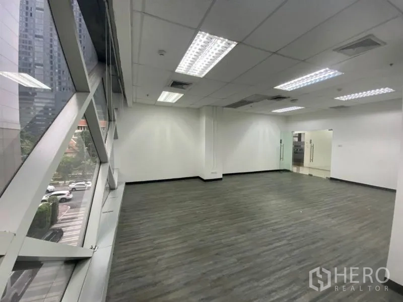 Office Space for rent in Khlong Toei, Bangkok - Spacious office interior with glass entry door, fluorescent lighting, and city outlook through wide windows.