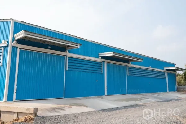 Warehouse for rent in Khlong Luang, Pathum Thani - Long blue warehouse facade with multiple sliding doors, awnings and a concrete ramp for truck access.