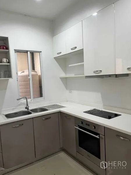 Townhouse for rent in Suan Luang, Bangkok - Compact L-shaped kitchen with white cabinets, sink and built-in oven.