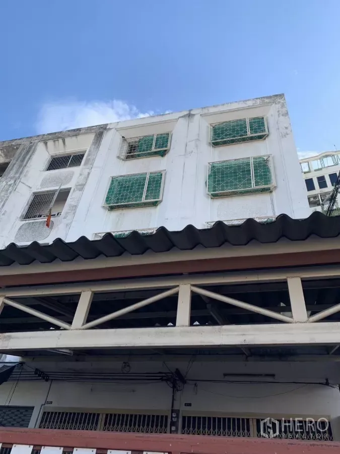Shophouse for rent in Suan Luang, Bangkok - Multi-storey shophouse facade with white exterior and green window grilles under a blue sky.