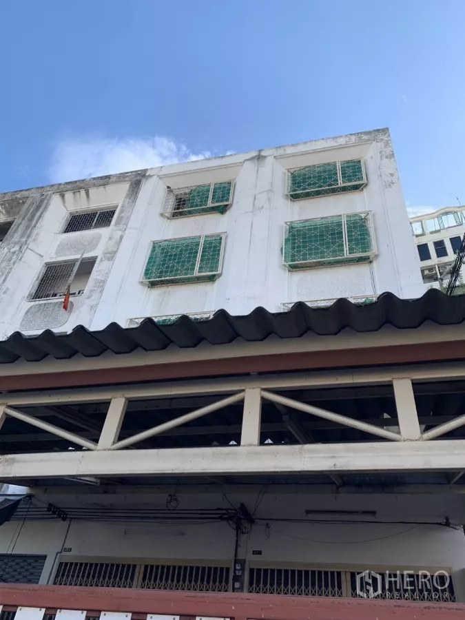 Shophouse for rent in Suan Luang, Bangkok - Multi-storey shophouse facade with white exterior and green window grilles under a blue sky.