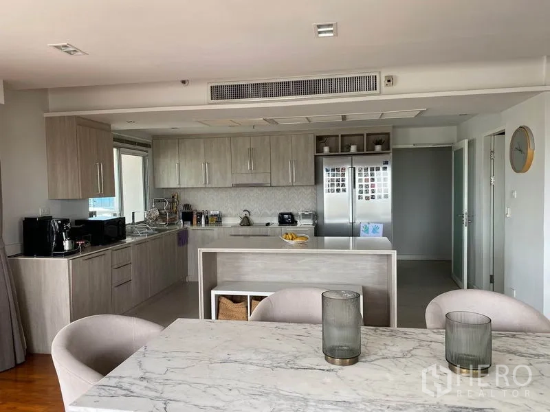 Condominium for rent in Sathon, Bangkok - Close-up of contemporary L-shaped kitchen with island, built-in cabinetry and double-door refrigerator.