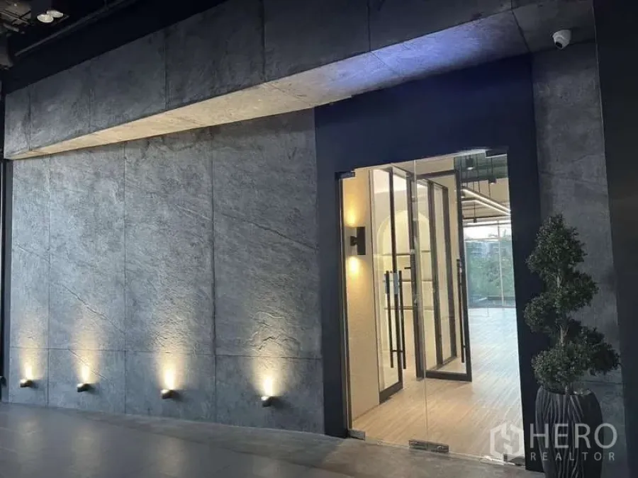Retail Space for rent - Modern glass storefront entrance set in a concrete feature wall with wall-washer lighting.