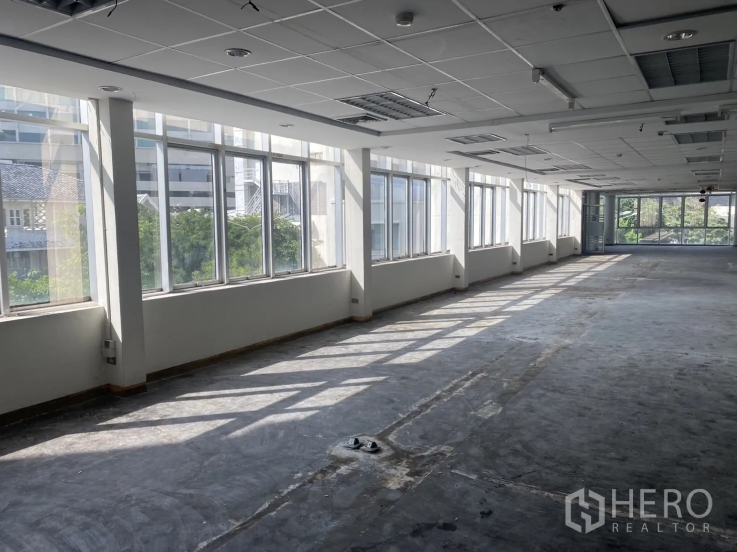 Office Space for rent in Khlong Toei, Bangkok - Long workspace with panoramic windows, raw concrete subfloor and leafy views, ready for fit-out.