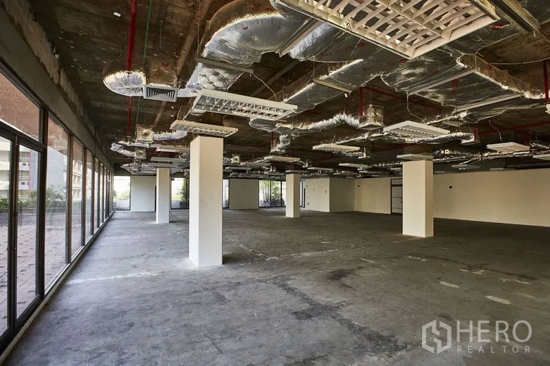 Office Space for rent in Bangkok - Large open-plan office shell with exposed ceiling ductwork, multiple columns and wall-to-wall windows.