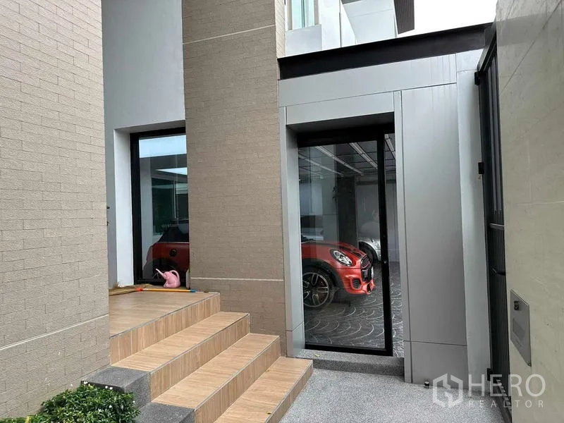 Detached House for sale in Suan Luang, Bangkok - Private entrance with tiled steps and a glass door looking into a covered carport with a red vehicle.