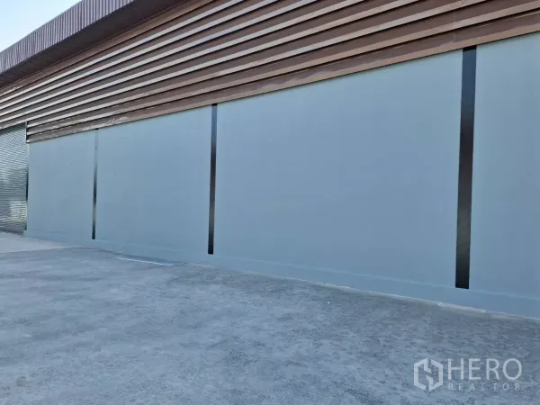 Factory for rent in Mueang Samut Sakhon, Samut Sakhon - Warehouse side elevation with metal cladding, roller shutter door and paved loading area.
