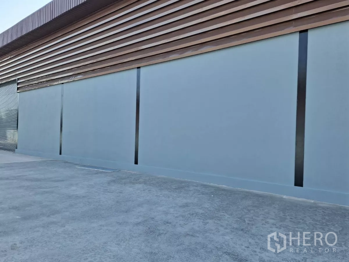 Factory for rent in Mueang Samut Sakhon, Samut Sakhon - Warehouse side elevation with metal cladding, roller shutter door and paved loading area.