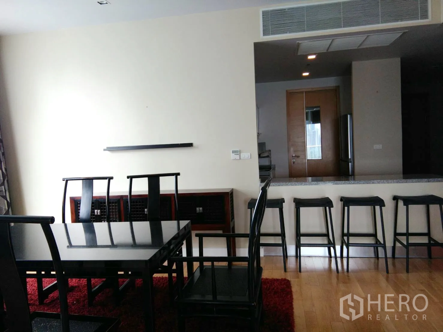 Condominium for rent in Khlong Toei, Bangkok - Dining area with black table, high-back chairs, and breakfast bar with stools.