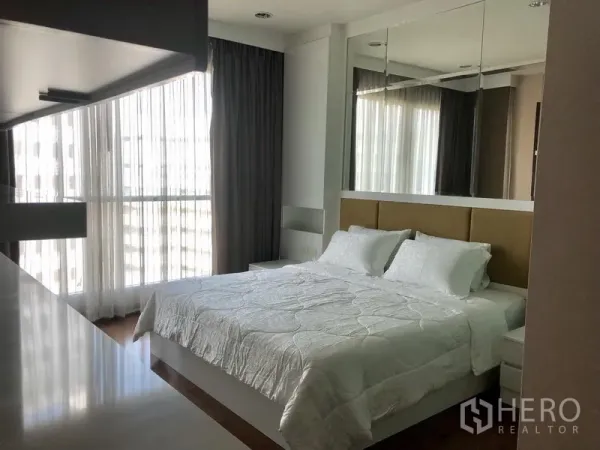 Condominium for rent in Pathum Wan, Bangkok - Spacious bedroom with a mirrored headboard wall, corner windows, and a large bed.