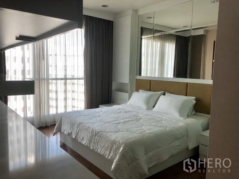 Condominium for rent in Pathum Wan, Bangkok - Spacious bedroom with a mirrored headboard wall, corner windows, and a large bed.