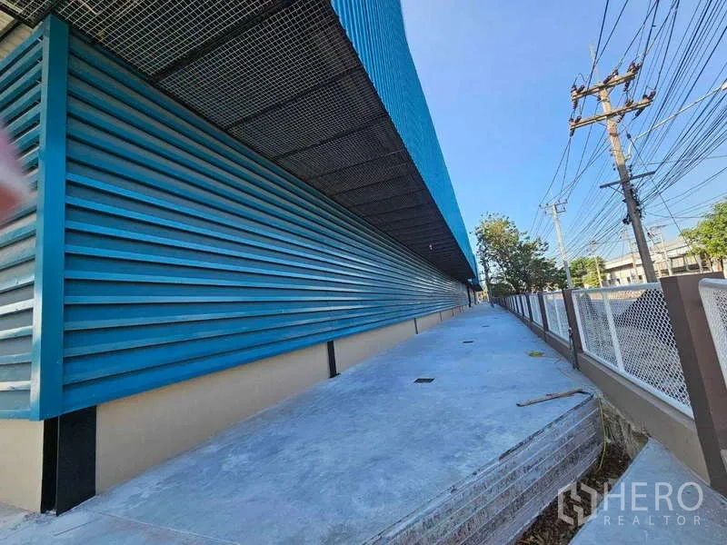 Factory for rent in Chon Buri - Long side loading platform under a metal awning beside blue cladding.