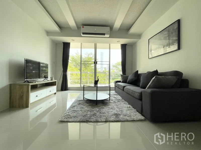 Condominium for rent in Khlong Toei, Bangkok - Living space facing balcony doors with sofa, TV unit, and treetop outlook.