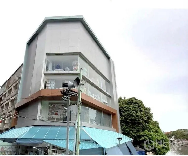 Shophouse for rent in Pathum Wan, Bangkok - Modern corner shophouse with full-height glass windows and a blue awning in Bangkok.