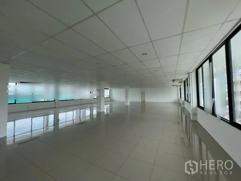 Office Space for rent - Expansive office hall with double rows of windows, suspended ceiling and reflective tiled floor, ideal for flexible layouts.