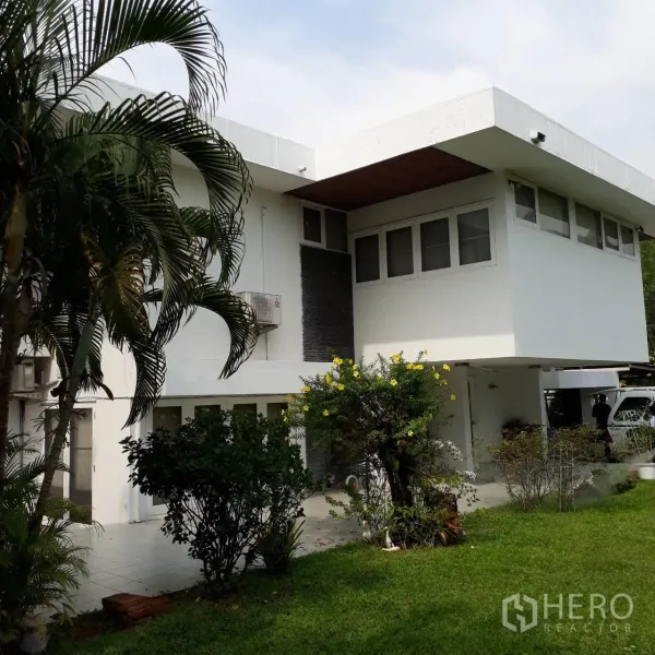 Detached House for rent in Khlong Toei, Bangkok - Two-storey white house with wide eaves, tiled terrace and tropical garden shrubs.