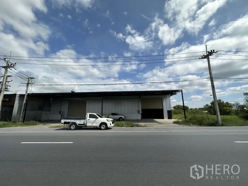 Warehouse for rent in Khlong Luang, Pathum Thani - Wide front elevation of long-span warehouse with multiple roller shutters and driveway off a main road.