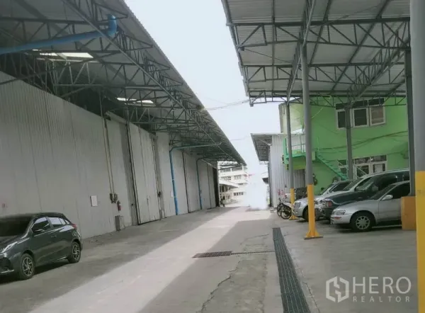 Warehouse for rent in Khlong Luang, Pathum Thani - Wide driveway between warehouse buildings with covered loading canopies and on-site parking spaces.